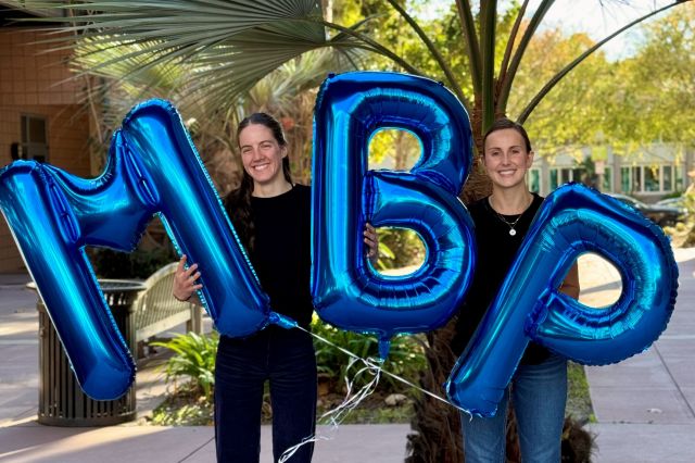 Photo of Kaya Jordan (left) and Hannah Grotzinger (right) holding balloons that say MBP